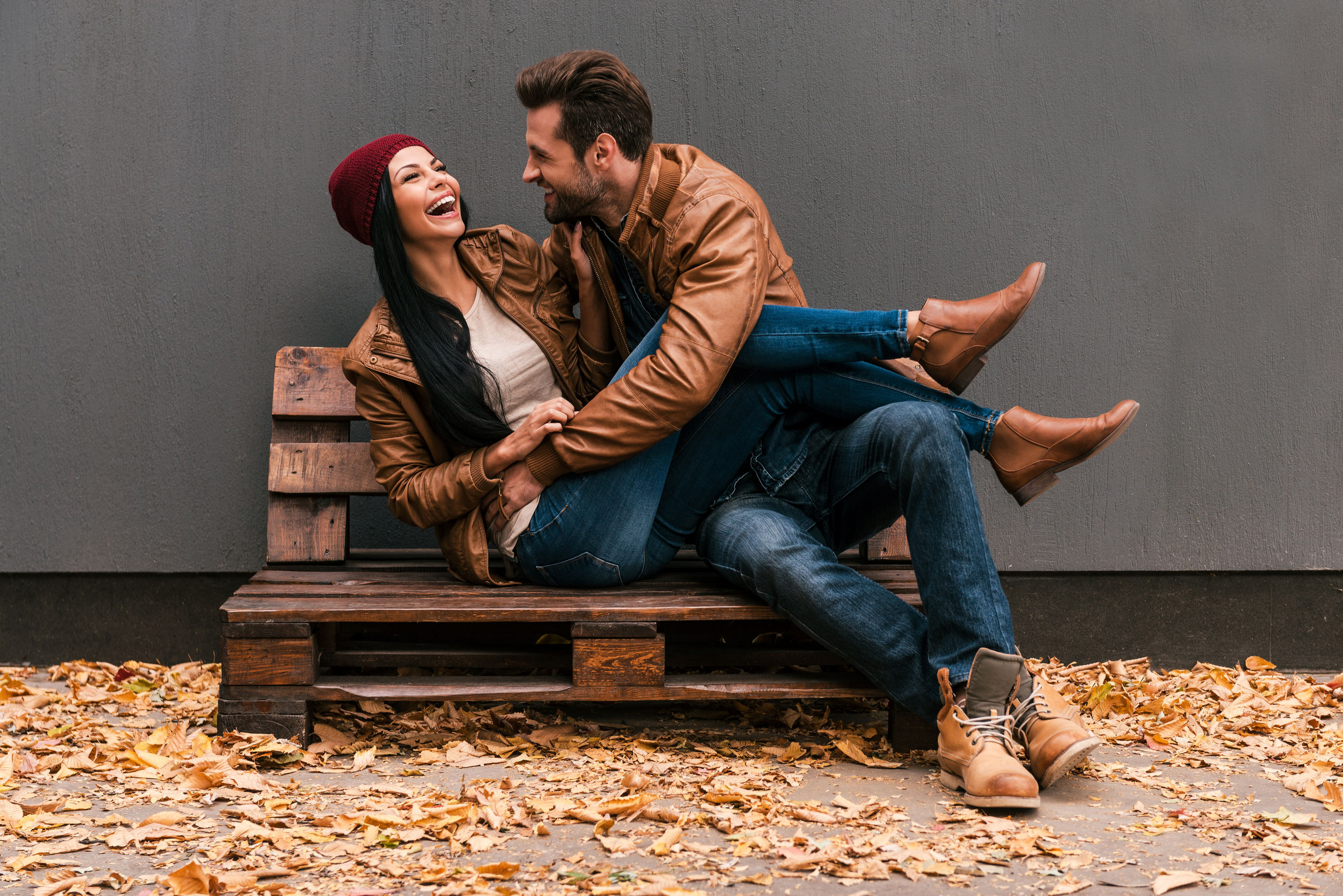 45974527 - carefree time together. beautiful young couple having fun together while sitting on the wooden pallet together with grey wall in the background and fallen leaves on ht floor